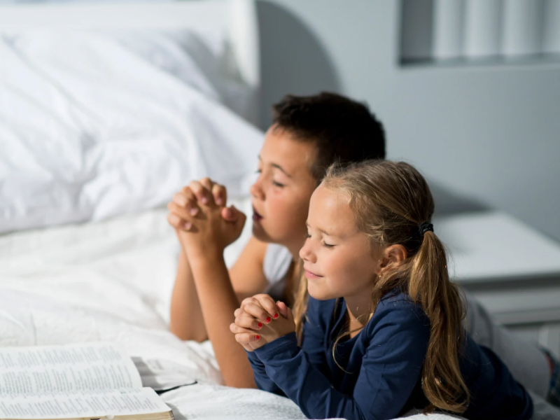 two children putting their hand together and praying