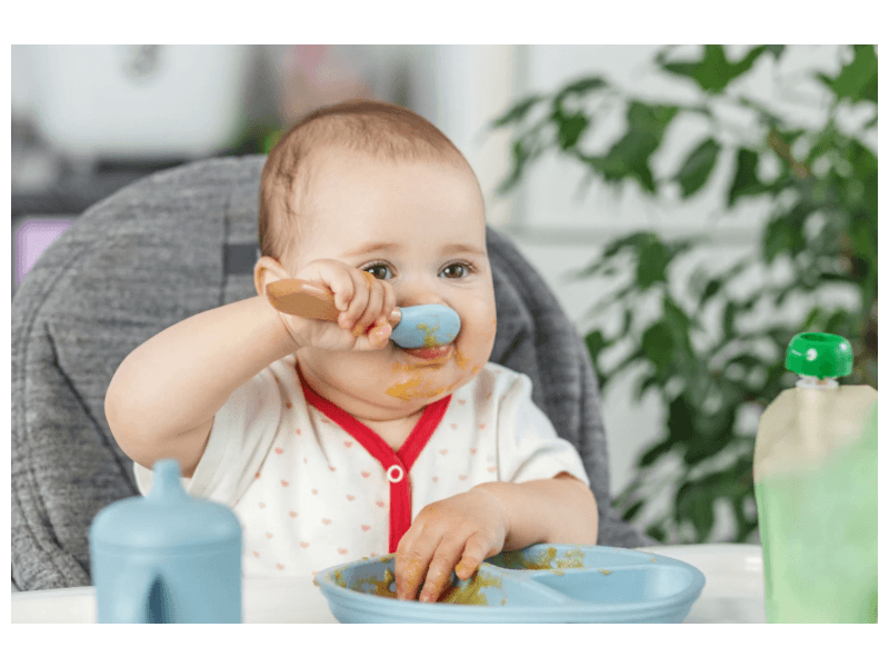 A chubby baby eating with a spoon in mouth